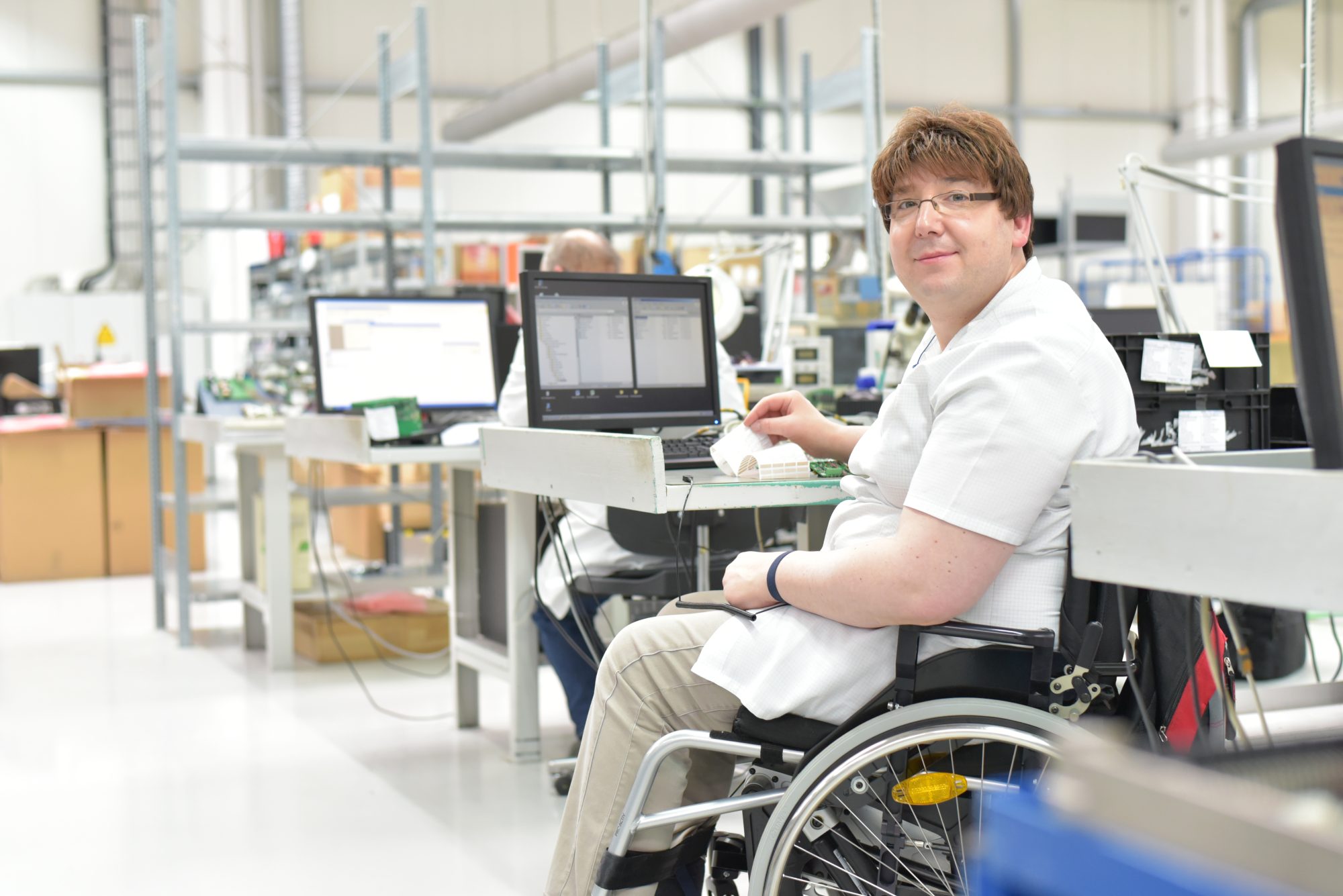 A person in a wheelchair works at a desk with a laptop in an industrial setting, highlighting inclusivity alongside issues like Race & National Origin Discrimination Mountain View and Pregnancy Leave Santa Rosa.