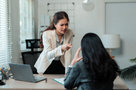 A woman in a white blazer is standing and pointing yelling at employee, to show hostile work environment Oakland.